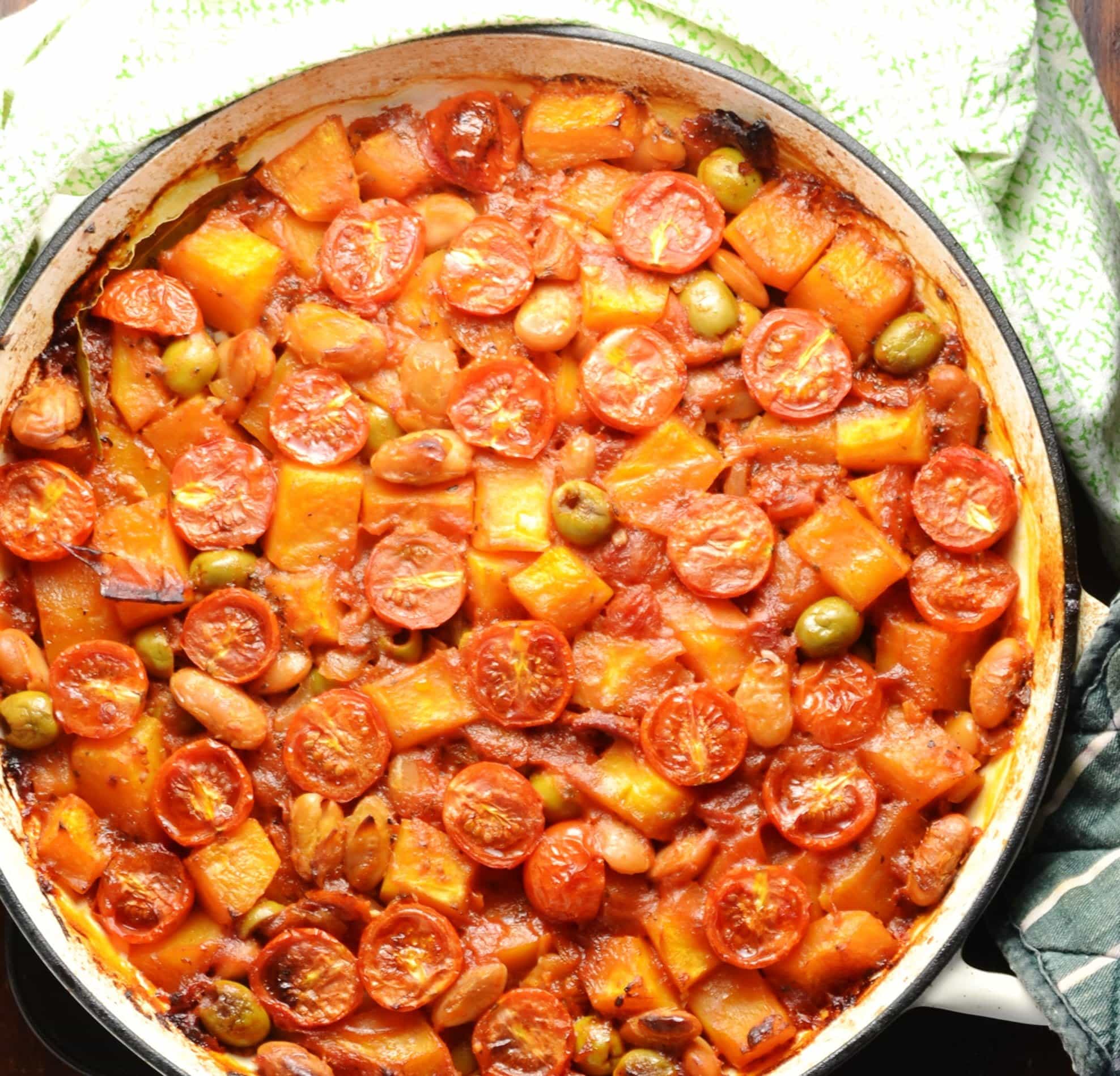 Top down view of butternut squash, cherry tomato and green olive casserole in large white dish.