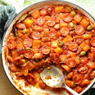 Top down view of butternut squash casserole in large shallow white dish with spoon and green cloth at top.