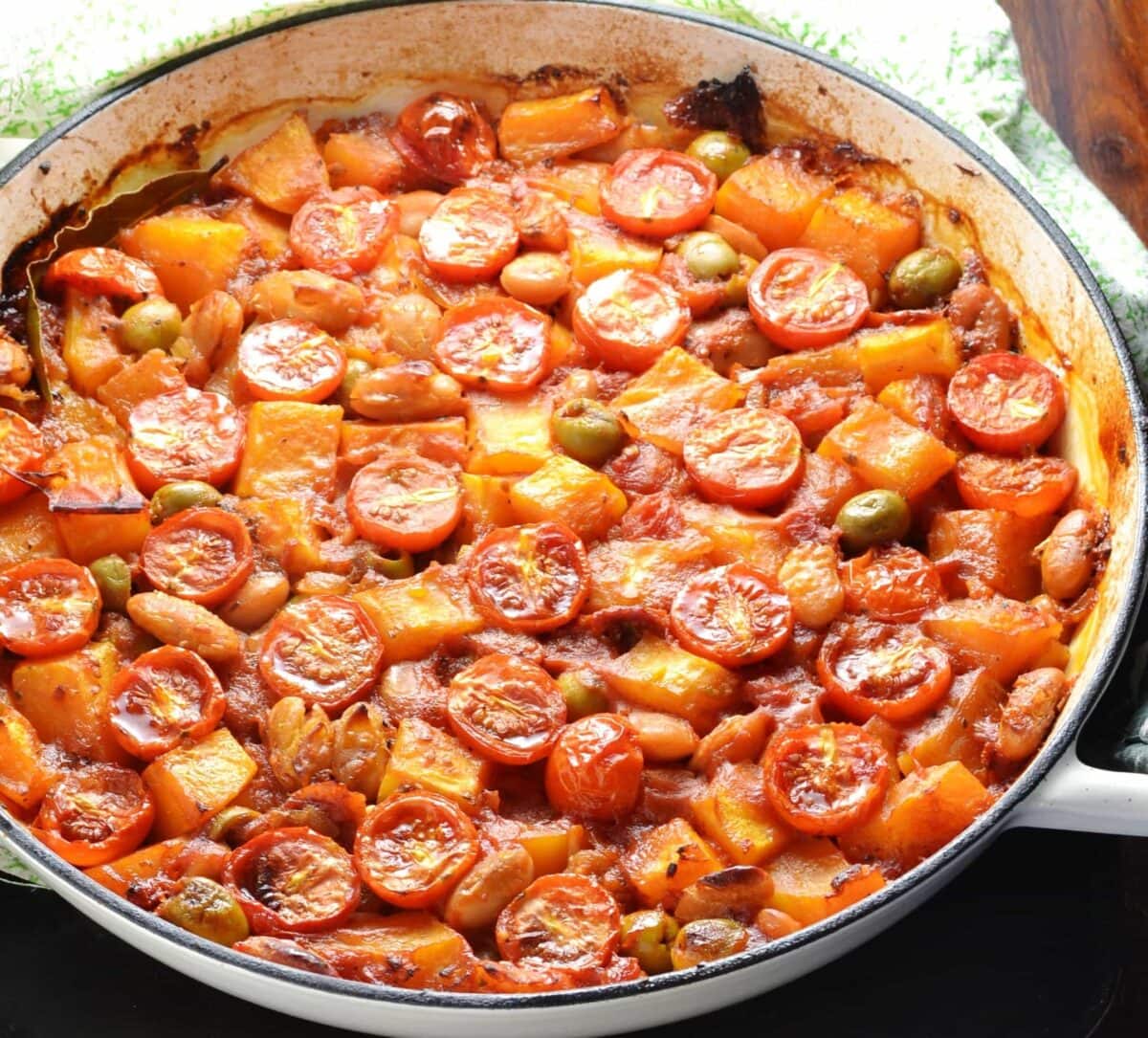 Close-up view of butternut squash casserole in large shallow white dish with green cloth at top.