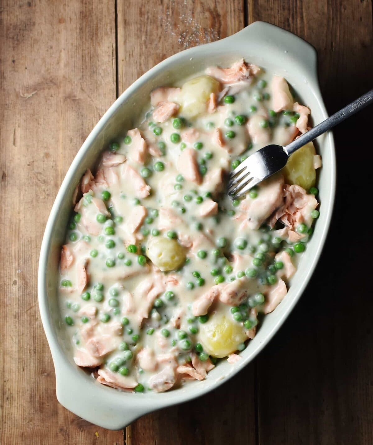 Creamy peas, salmon and potatoes in oval, white casserole dish with fork.