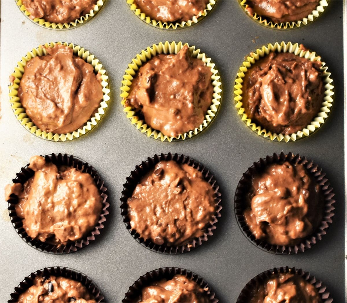 Pumpkin muffin batter in paper liners in muffin pan.