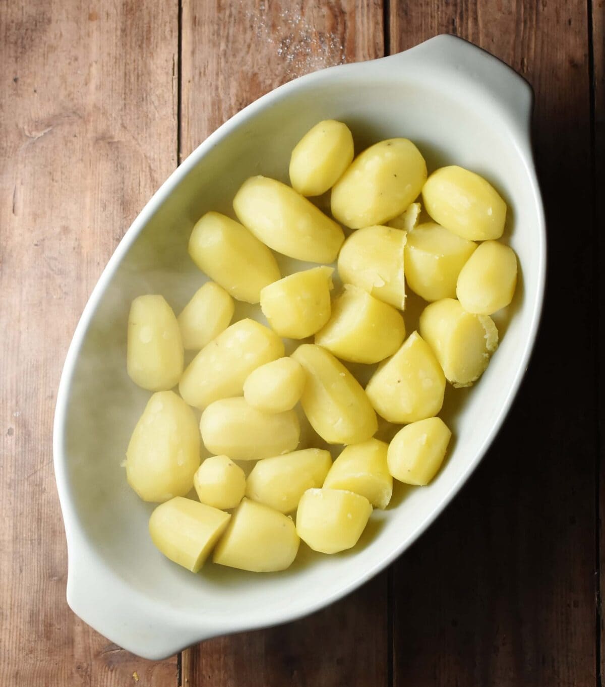 Steaming peeled potatoes in oval, white casserole dish.