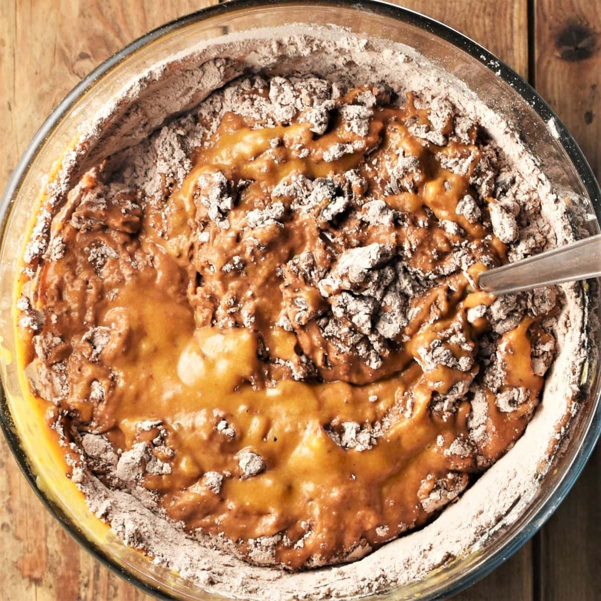Pumpkin mixture with flour and chocolate chips in mixing bowl with spoon.