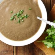 Top down view of creamy mushroom potato soup with herbs in white bowl with spoon, herbs to the right and pot with soup at the top.