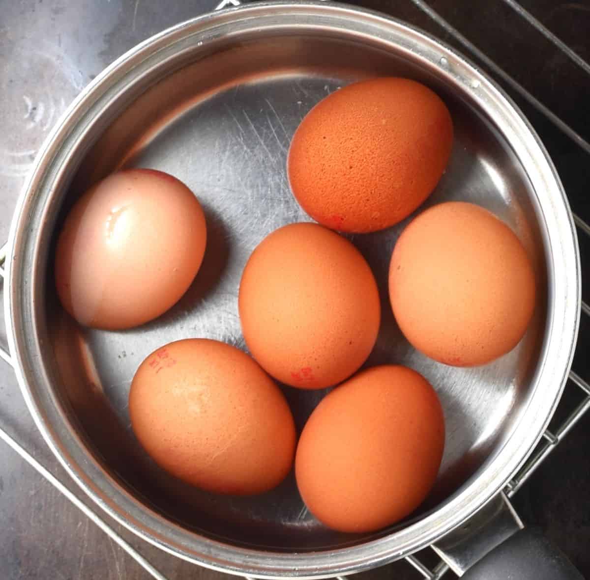 Top down view of 6 eggs in pot with water.