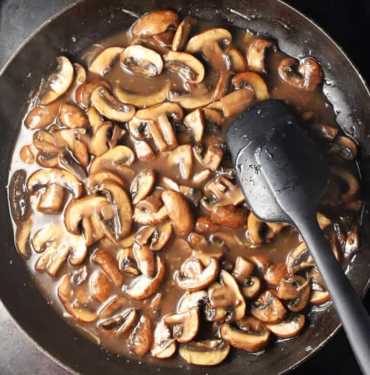 Chopped mushrooms in sauce with black spatula in pan.