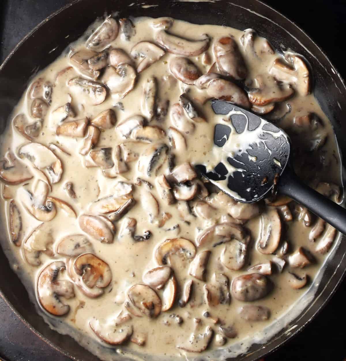 Mushrooms in creamy sauce for pasta in pan with spoon.