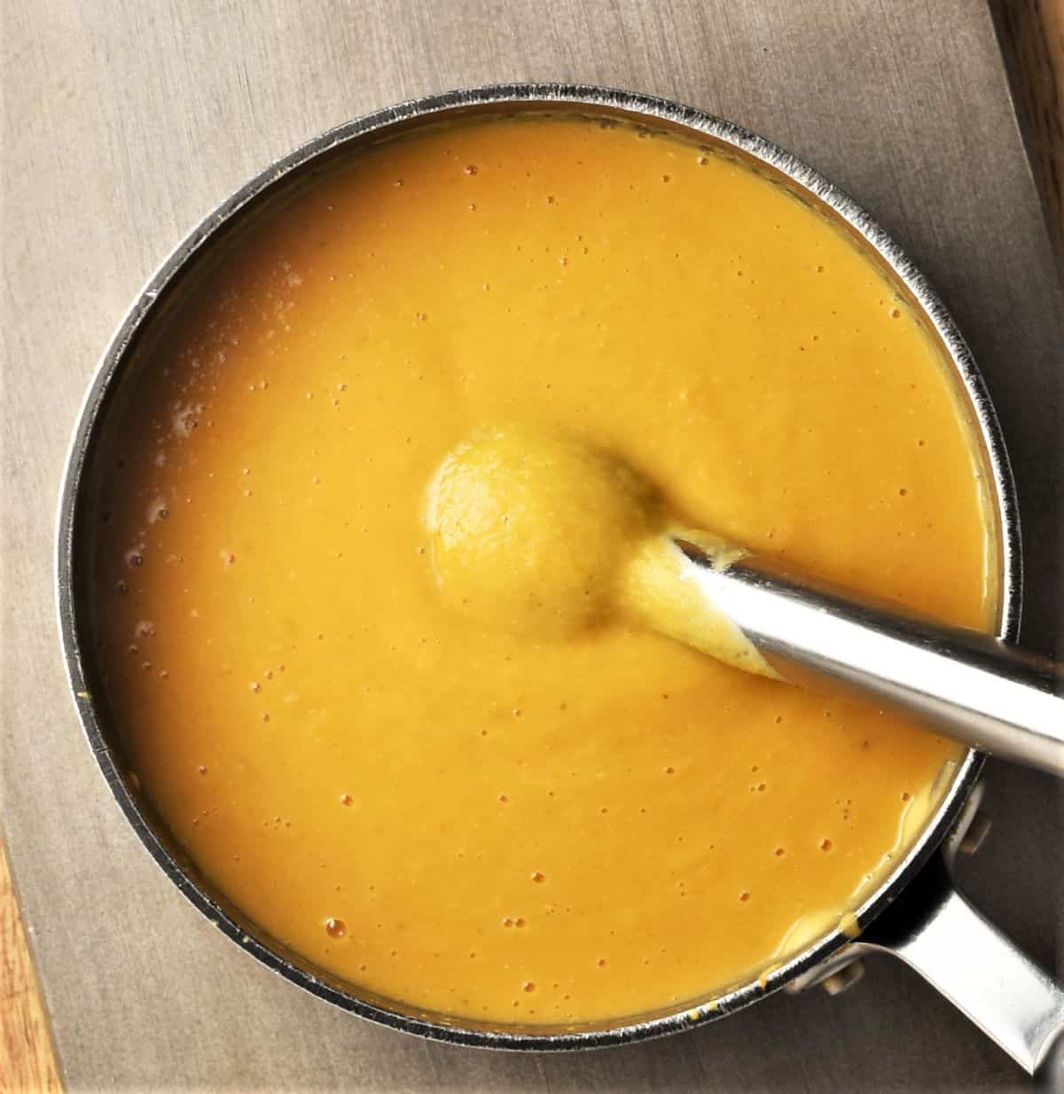 Pureeing lentil butternut squash soup with stick blender until creamy in pot.