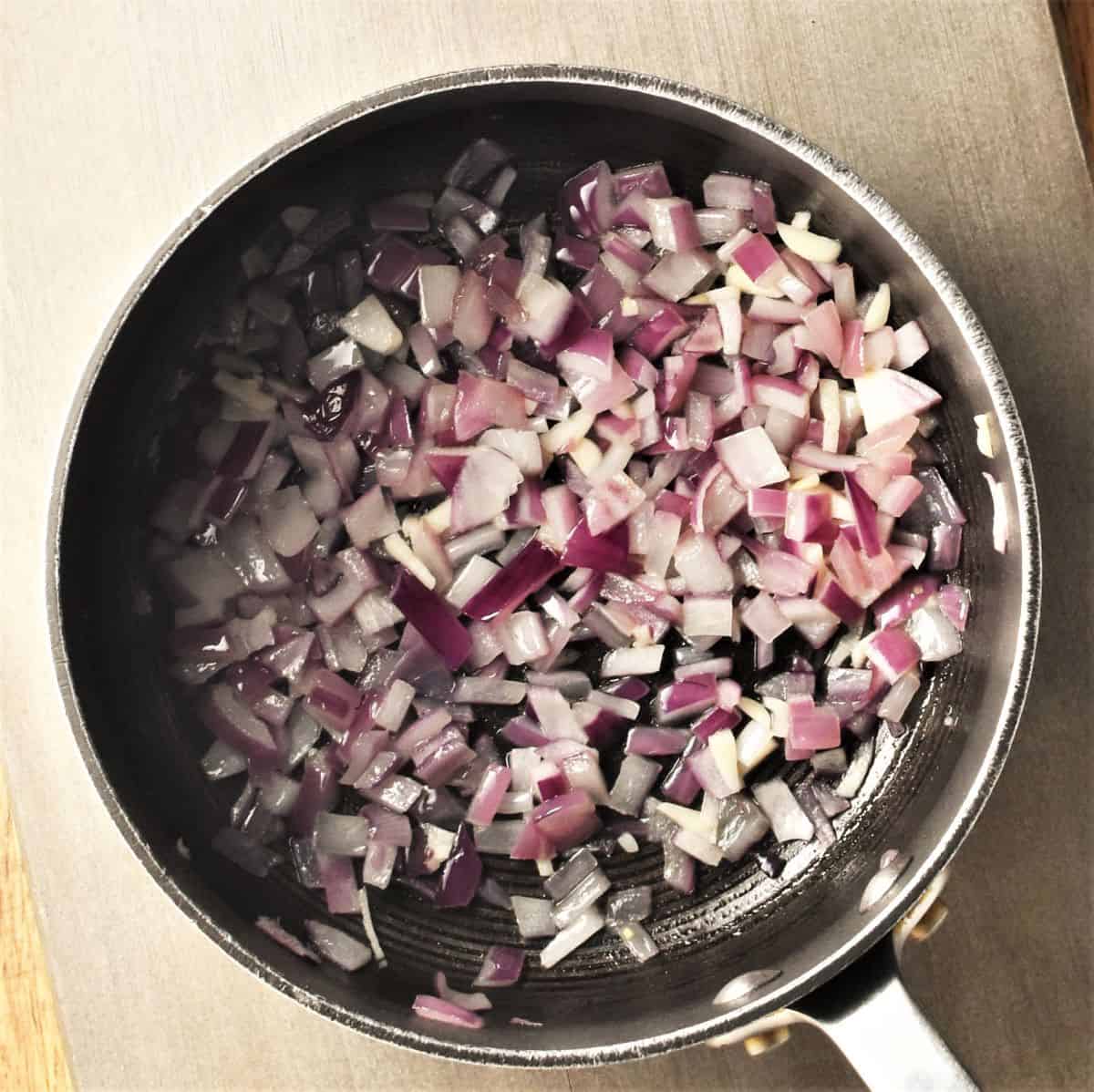 Frying chopped red onion in pot.