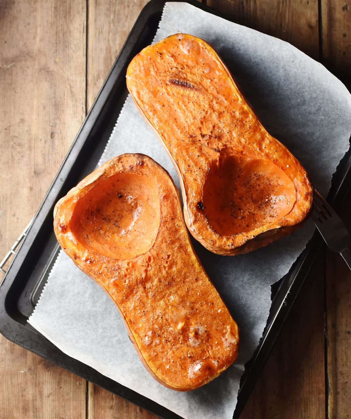 Roasted butternut squash halves on top of baking sheet lined with parchment paper.