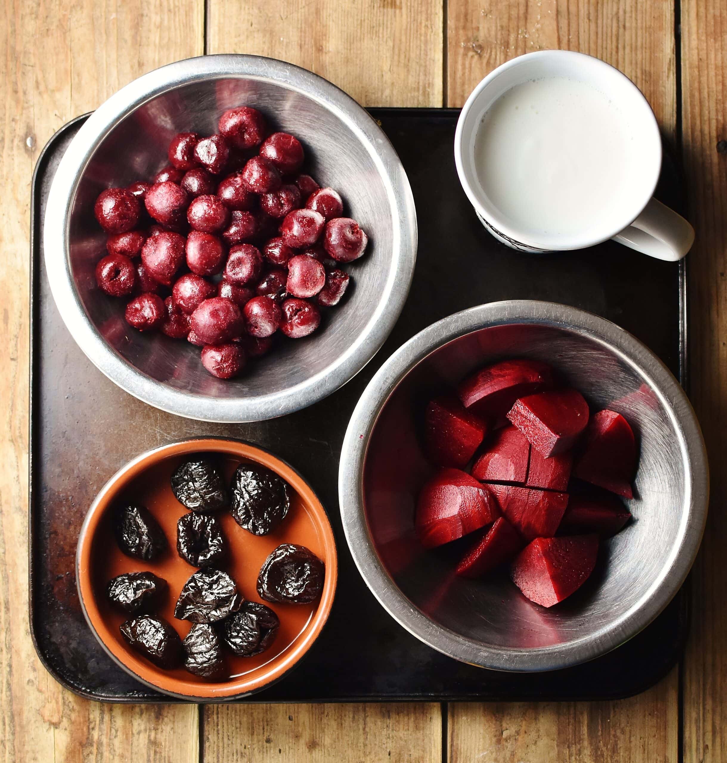 Cherries, cubed beetroot and prunes in separate bowls and kefir in cup.