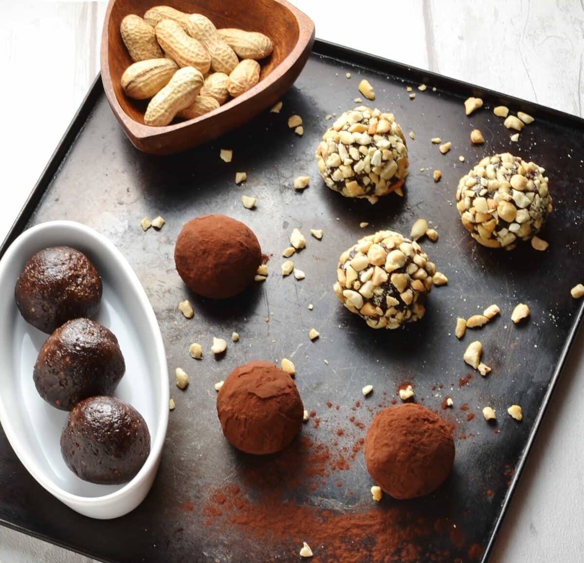 Chocolate energy balls coated with cocoa and crushed peanuts on top of oven tray with white oval dish.