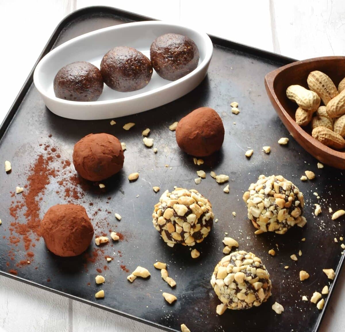 Side view of chocolate energy balls coated in cocoa and crushed nuts on metallic tray.