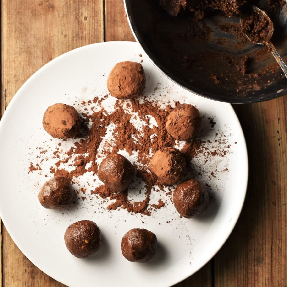 Chocolate balls on top of white plate with cocoa powder and bowl in top right corner.