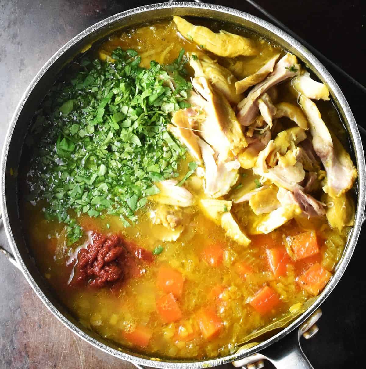Mulligatawny chicken soup with herbs and vegetables in large pot.