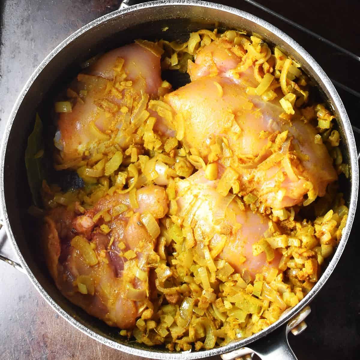 Chicken thighs with chopped onion and spices in pot.