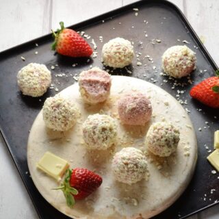 Strawberry cheesecake balls on round marble plate with strawberries and white chocolate on oven tray.