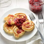 Polish pancakes on white plate with raspberry compote and forks on white table.