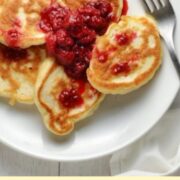 Top down view of pancakes with fruit compote and fork on top of white plate.