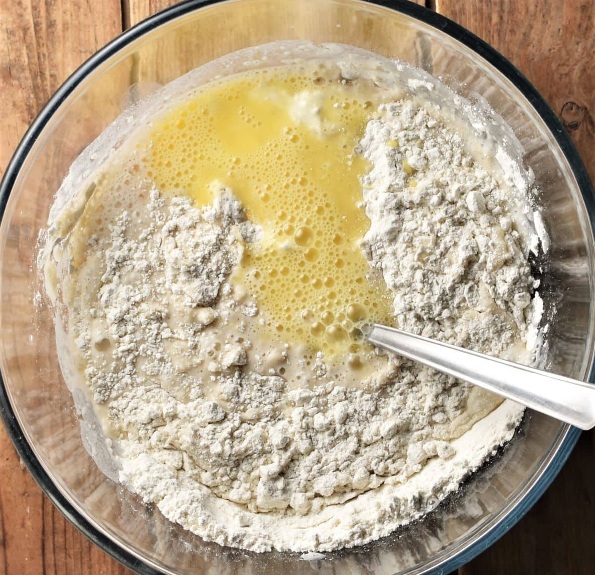 Combining racuchy ingredients in mixing bowl with spoon.