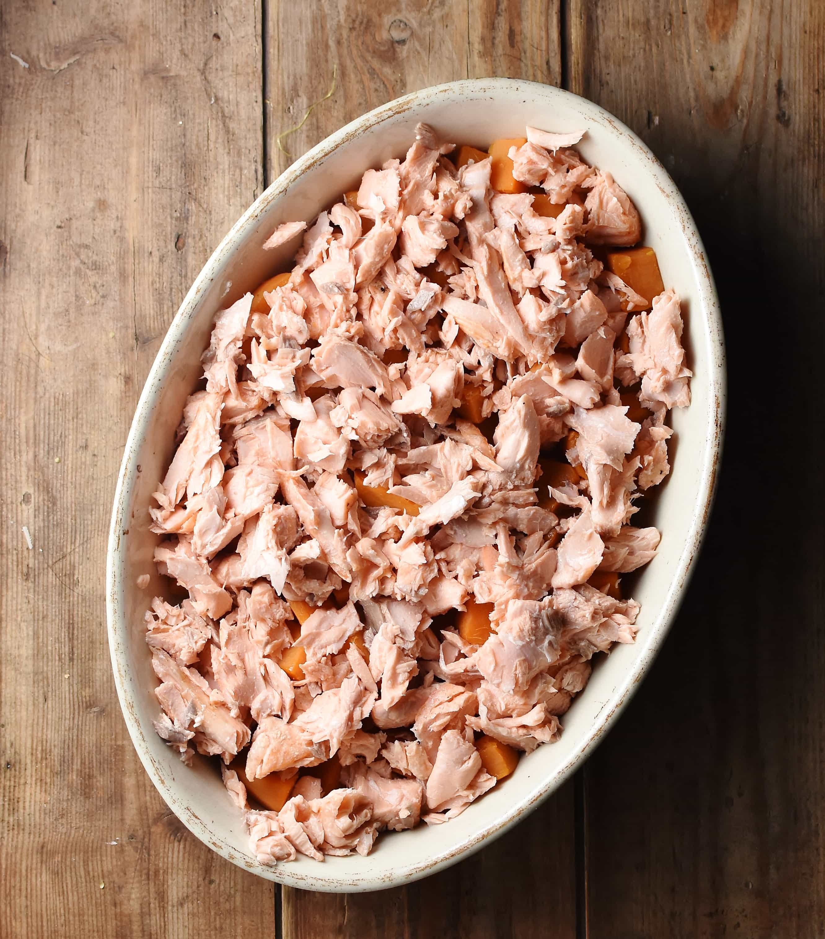 Salmon pieces scattered over sweet potato in white oval dish.