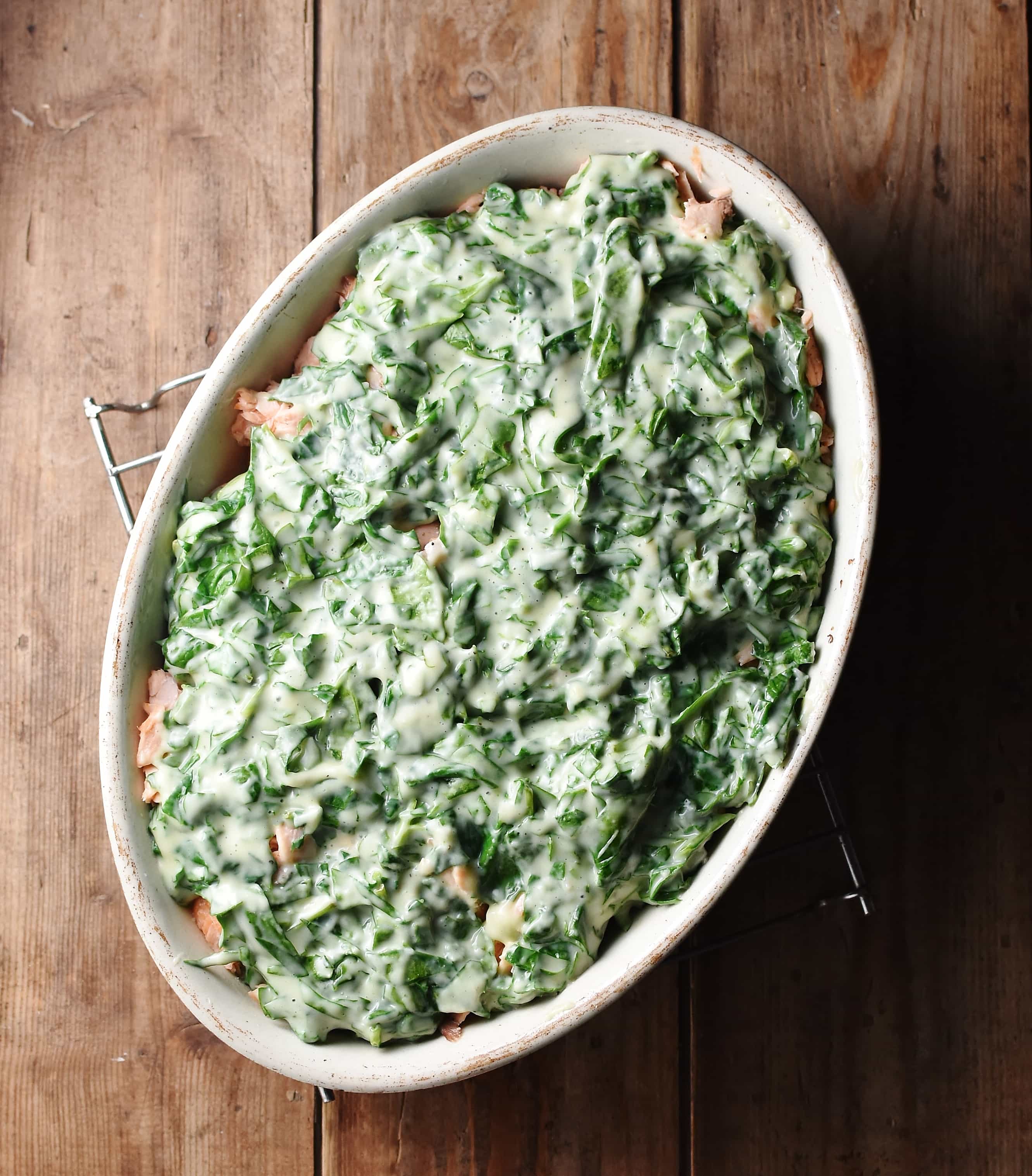 Pie with spinach in creamy white sauce on top in white oval dish.