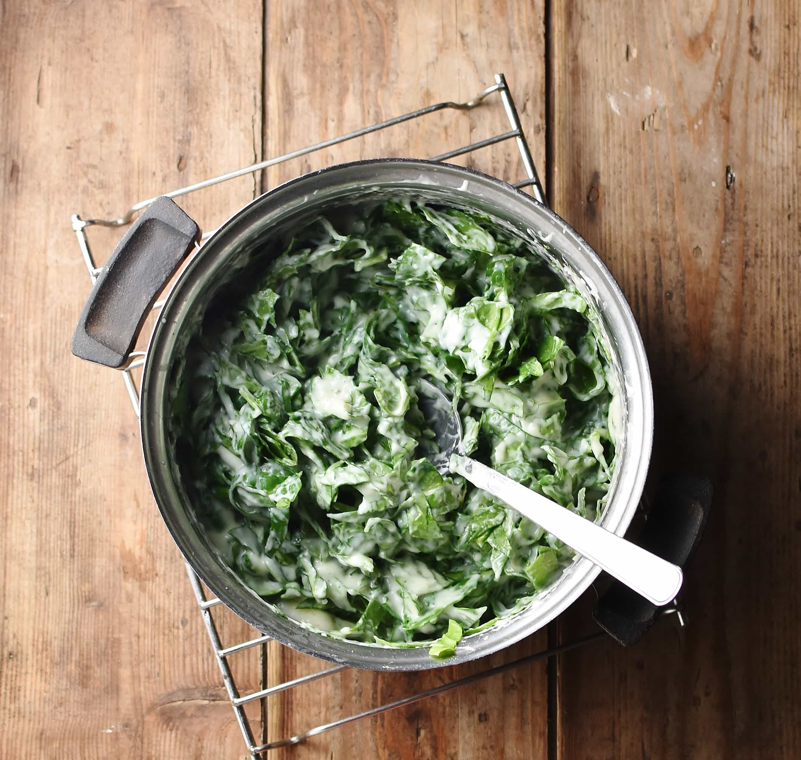 Chopped spinach with white sauce in pot with spoon.
