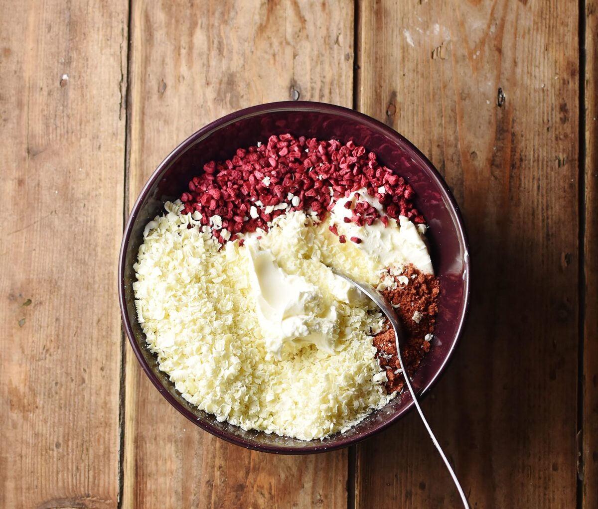 While chocolate shavings, cream cheese, chopped freeze dried strawberries and spoon in purple bowl.
