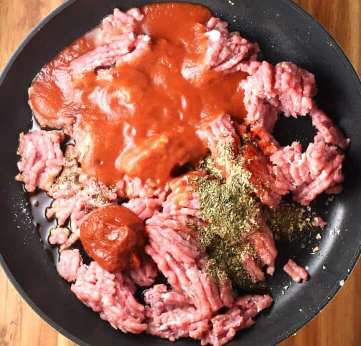 Top down view of ground meat with spices and tomato puree in large pan.