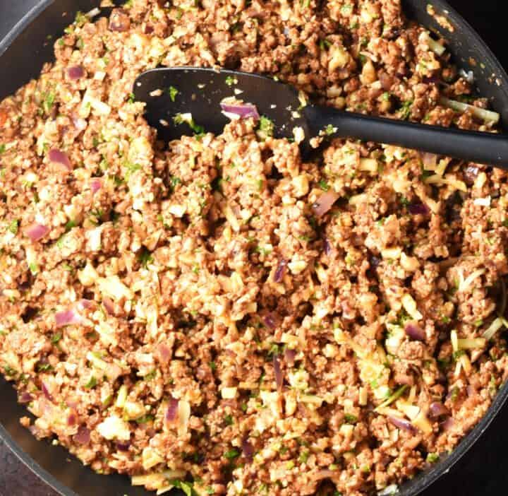 Cauliflower rice and meat filling mixture for peppers with black spatula in pan.