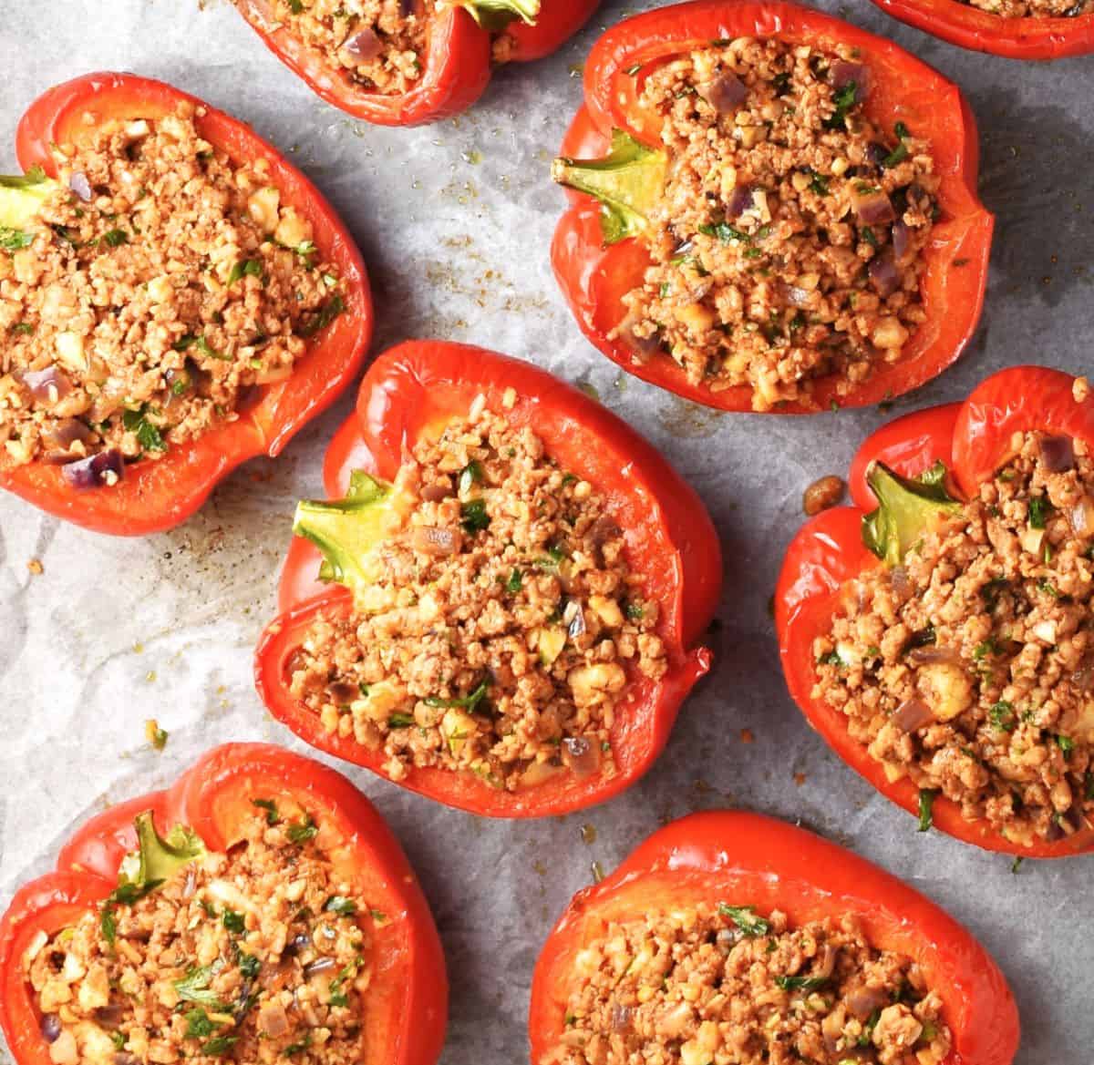 Pepper halves filled with cauliflower meat stuffing mixture on parchment.