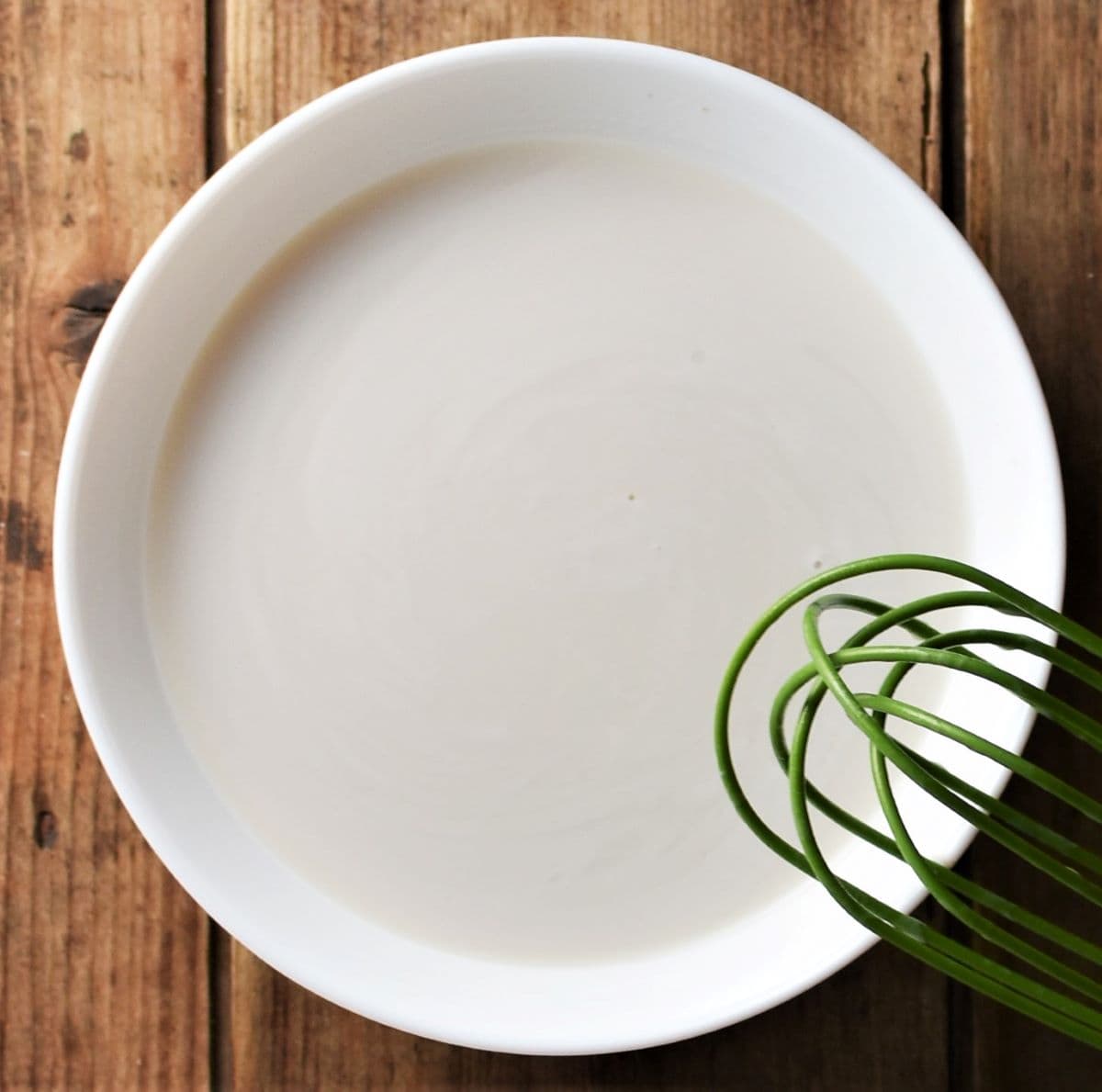 Milk mixture in white bowl with green whisk.