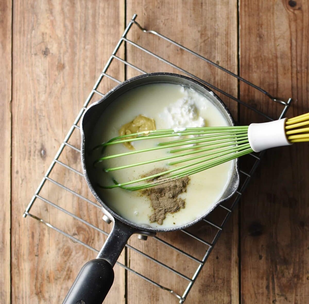 White sauce with mustard, yogurt, spices and green whisk in small saucepan.