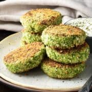 Side view of crispy broccoli patties stacked on plate.