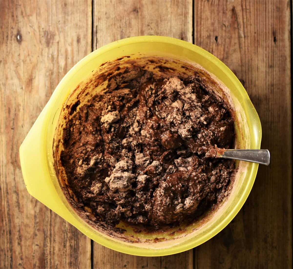 Brownies batter with some flour visible in large yellow bowl with spoon.