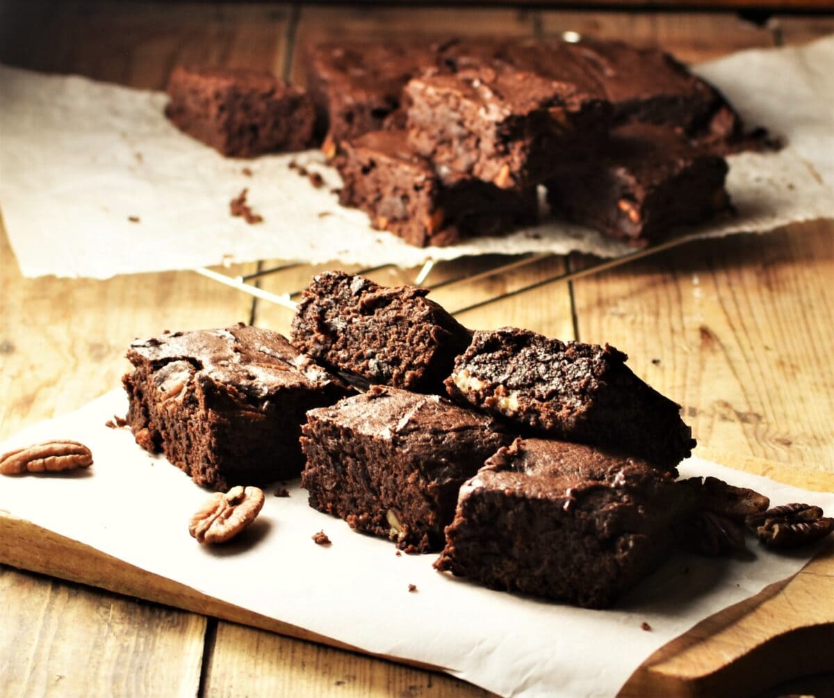 Sweet potato brownies on top of paper with pecans and brownies in background on cooling rack.