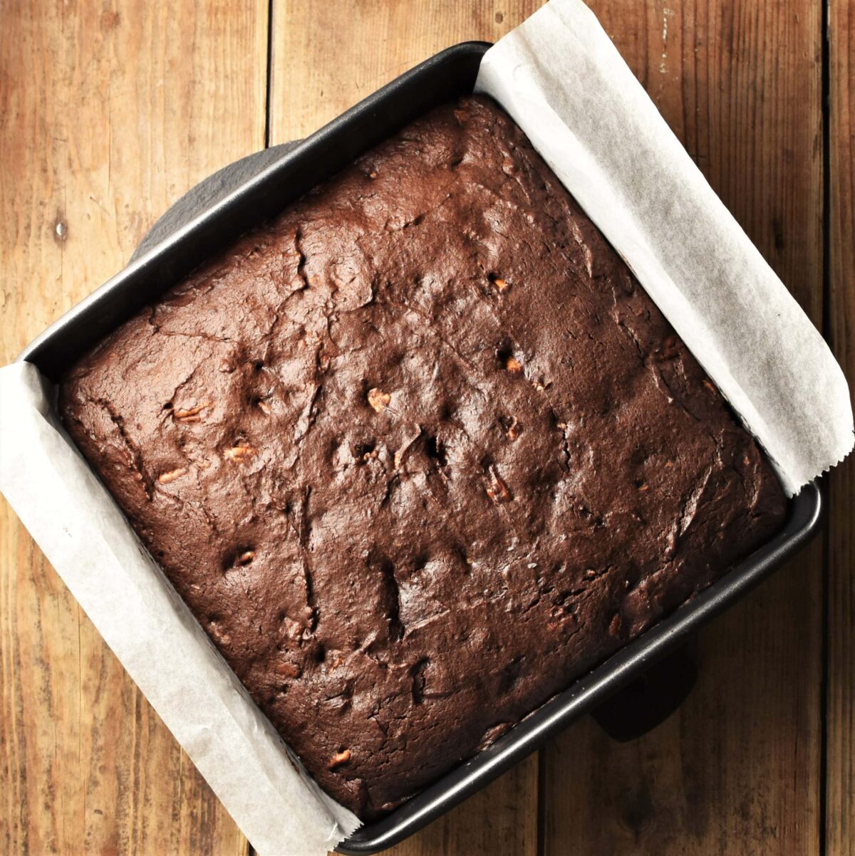 Top down view of brownie cake in square pan lined with paper.