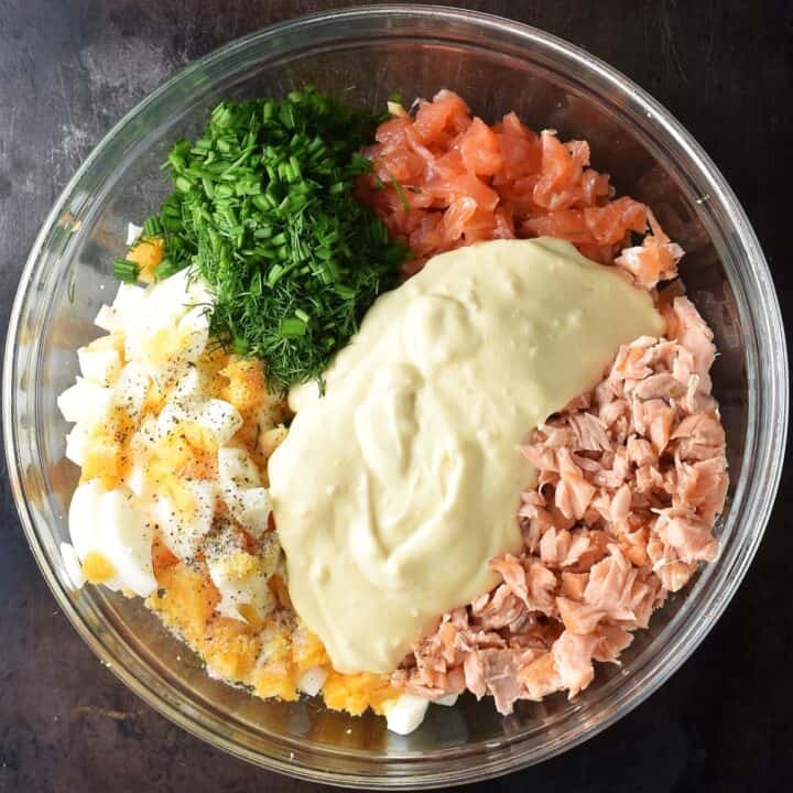 Top down view of ingredients for egg salmon salad in glass bowl.