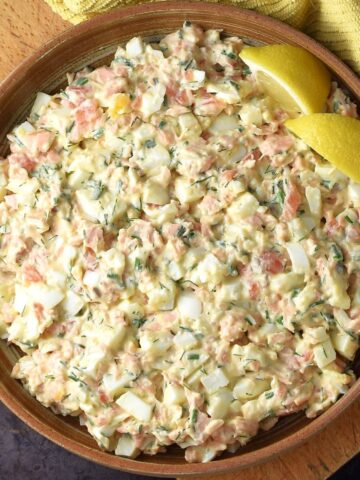 Top down view of creamy salmon egg salad with lemon wedges in brown bowl.