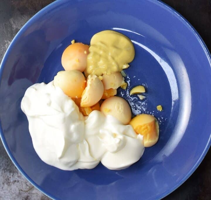 Cooked egg yolks with mayonnaise and mustard in blue bowl.
