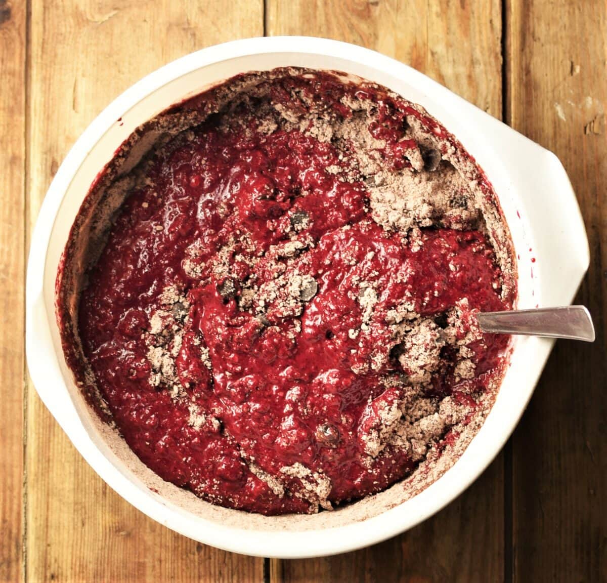 Beetroot muffin batter with some flour visible in large white bowl with spoon.