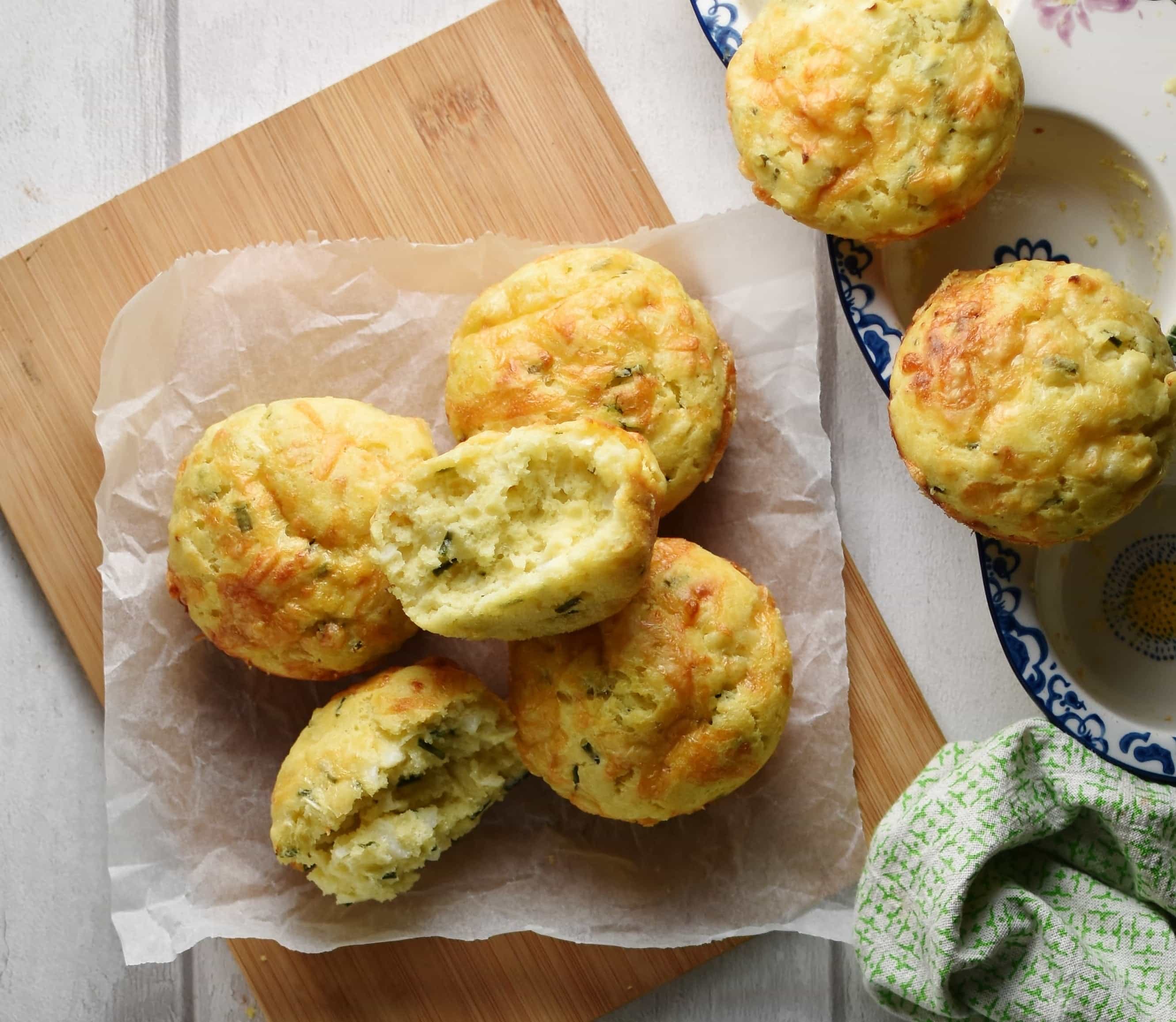 Top down view of muffins on top of wooden board lined with baking paper, with green cloth to the right.