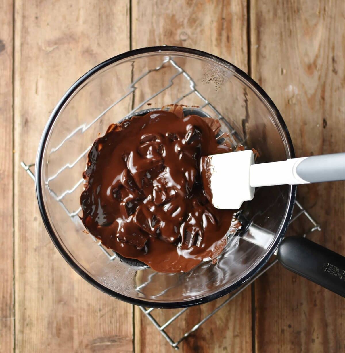 Melted chocolate with white plastic spatula in see-through glass bowl.