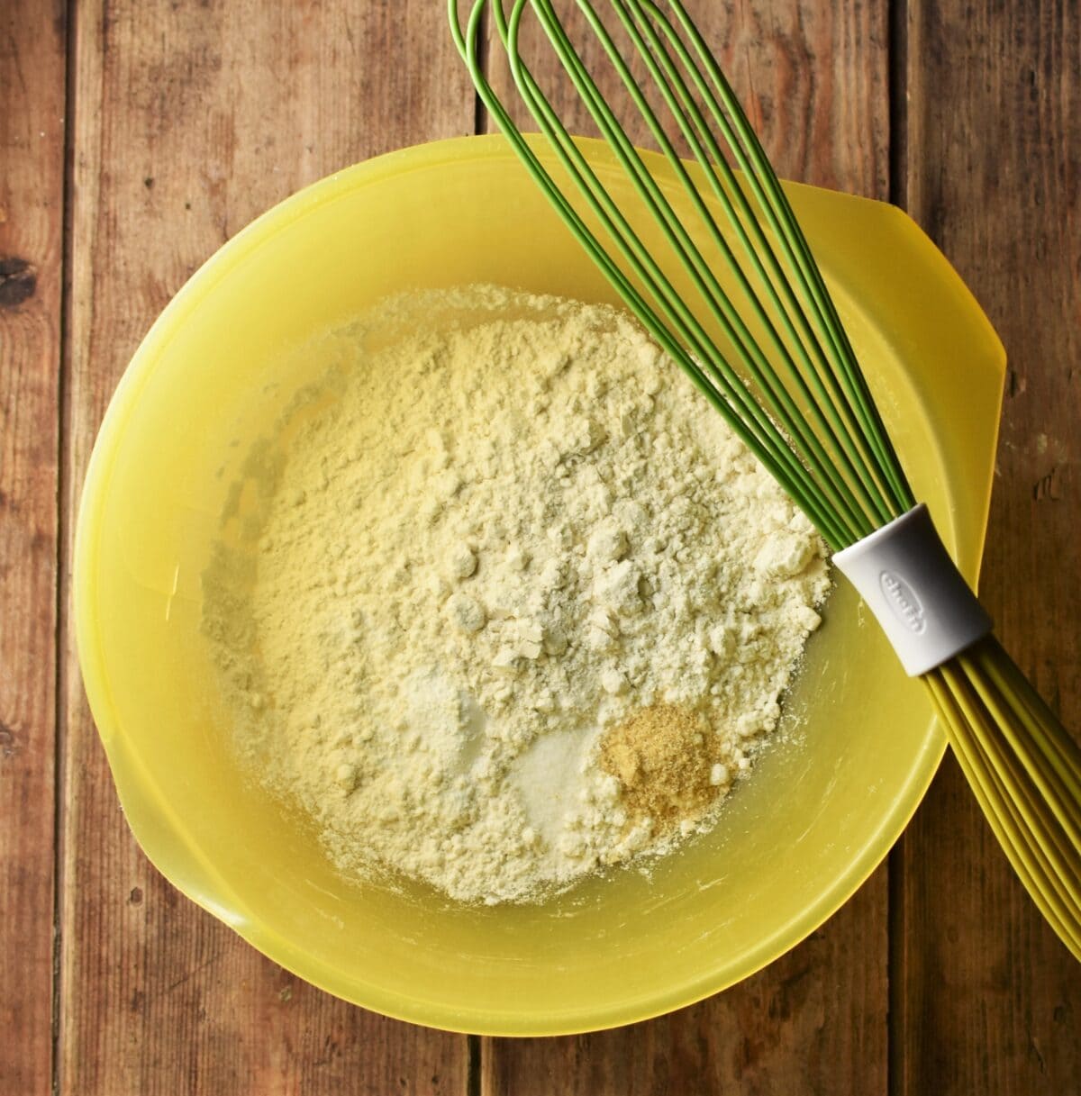 Flour mixture in large yellow bowl with green whisk.