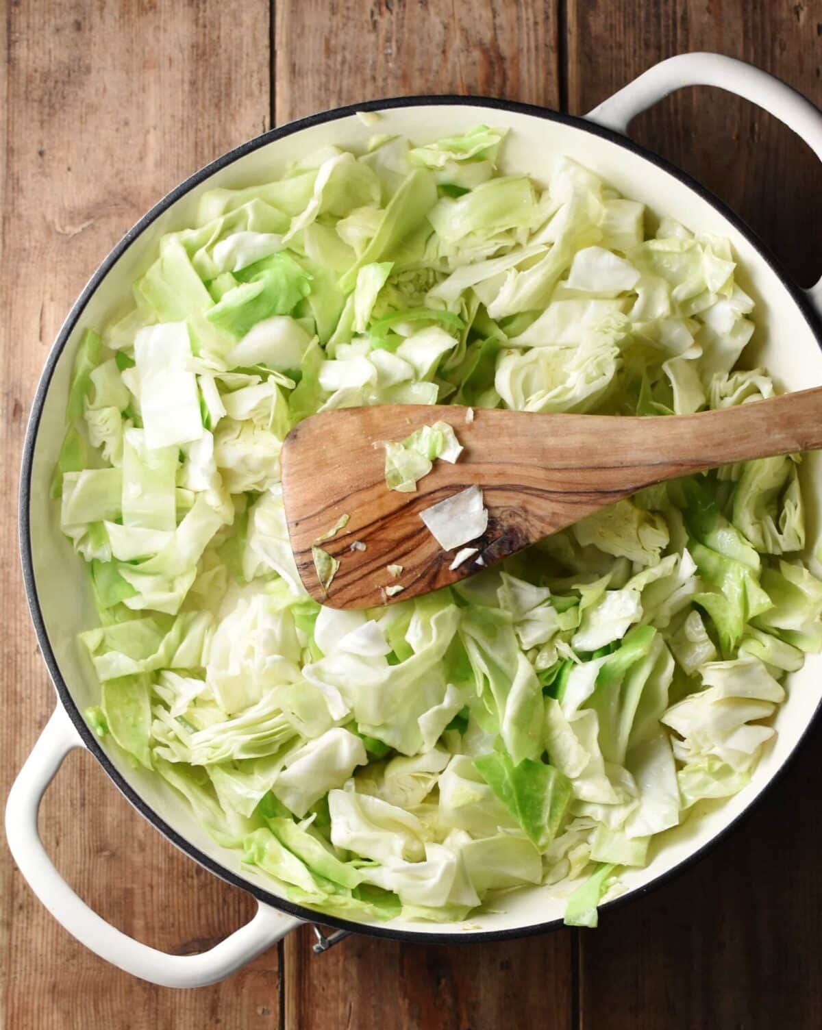 Chopped cabbage in large white dish with wooden spatula.