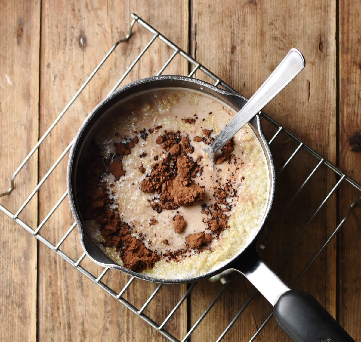 Quinoa with milk and cocoa powder in saucepan with spoon.