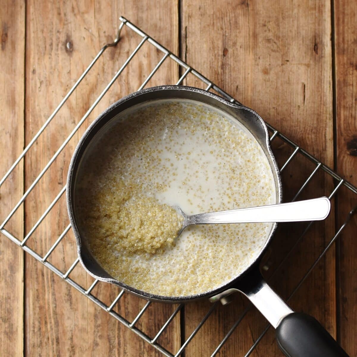 Quinoa with milk in saucepan with spoon.