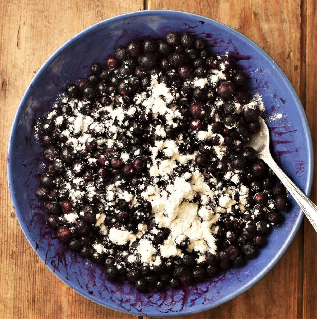 Blueberries with flour in blue bowl with spoon.