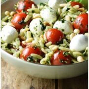 Close-up partial view of orzo pesto salad with cherry tomatoes and mozzarella balls inside light green bowl.