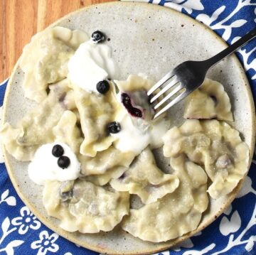 Top down view of blueberry pierogi with sour cream on plate with fork.